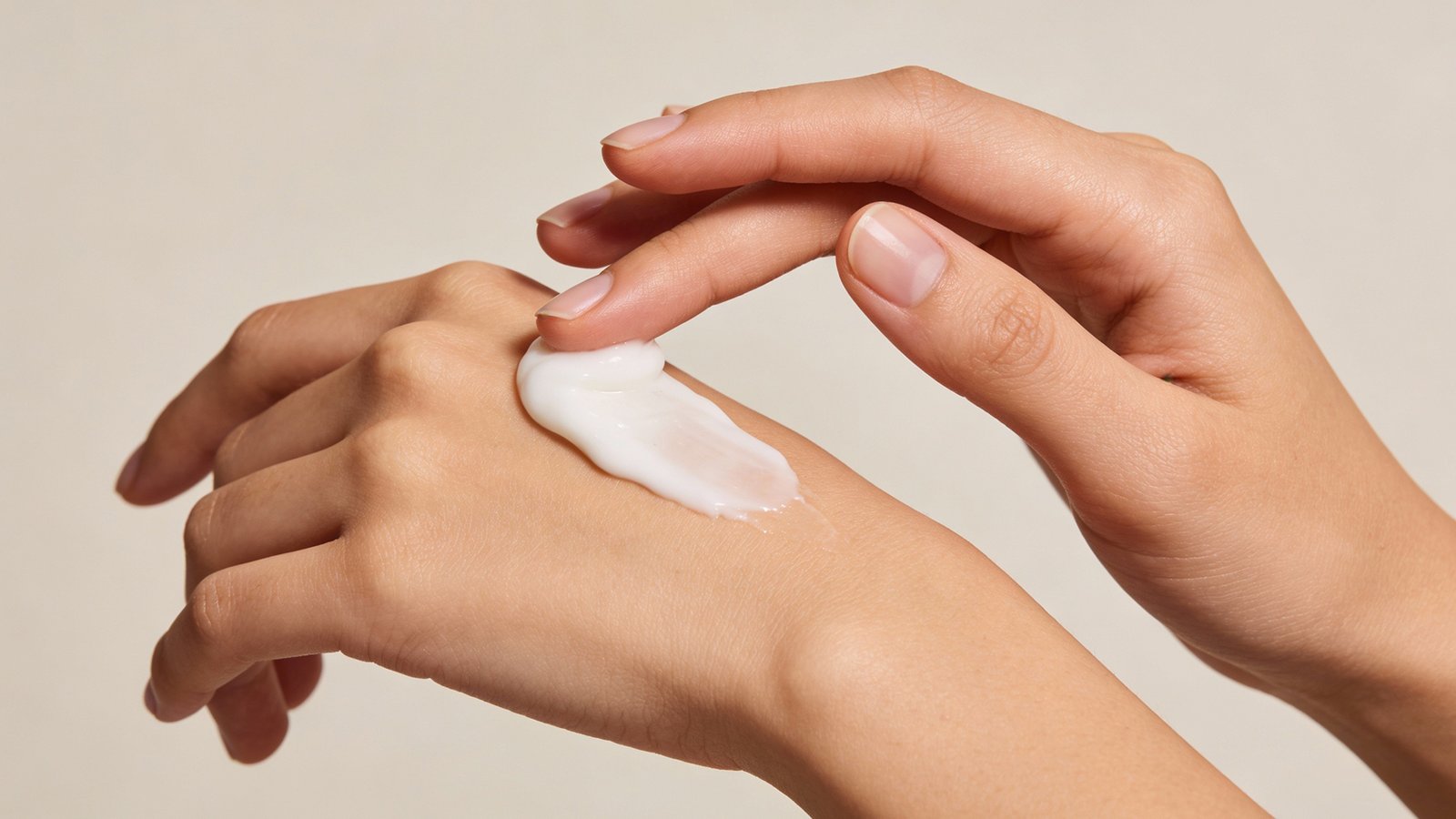 Tangan sedang memegang moisturizer dan mengapply sedikit di bagian belakang tangan